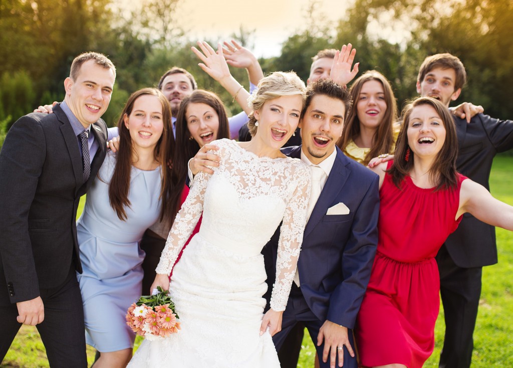 Portrait of newlywed couple having fun with bridesmaids and groomsmen in green sunny park