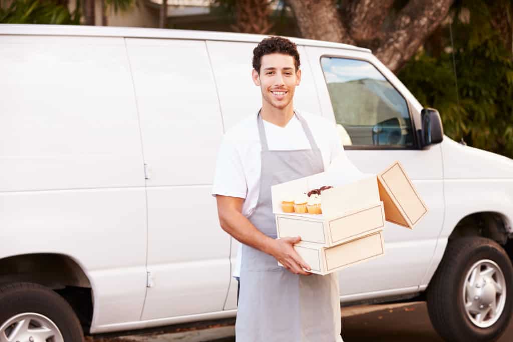 Man holding cakes while standing beside a van.